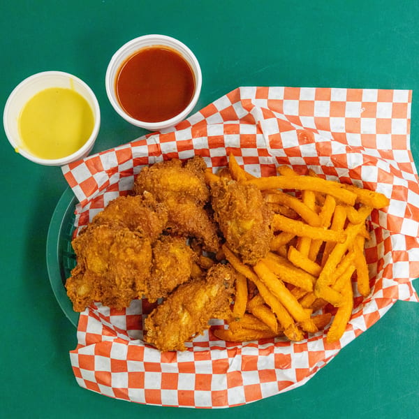 Golden fried chicken wings and sweet potato fries in a basket with two sauces.