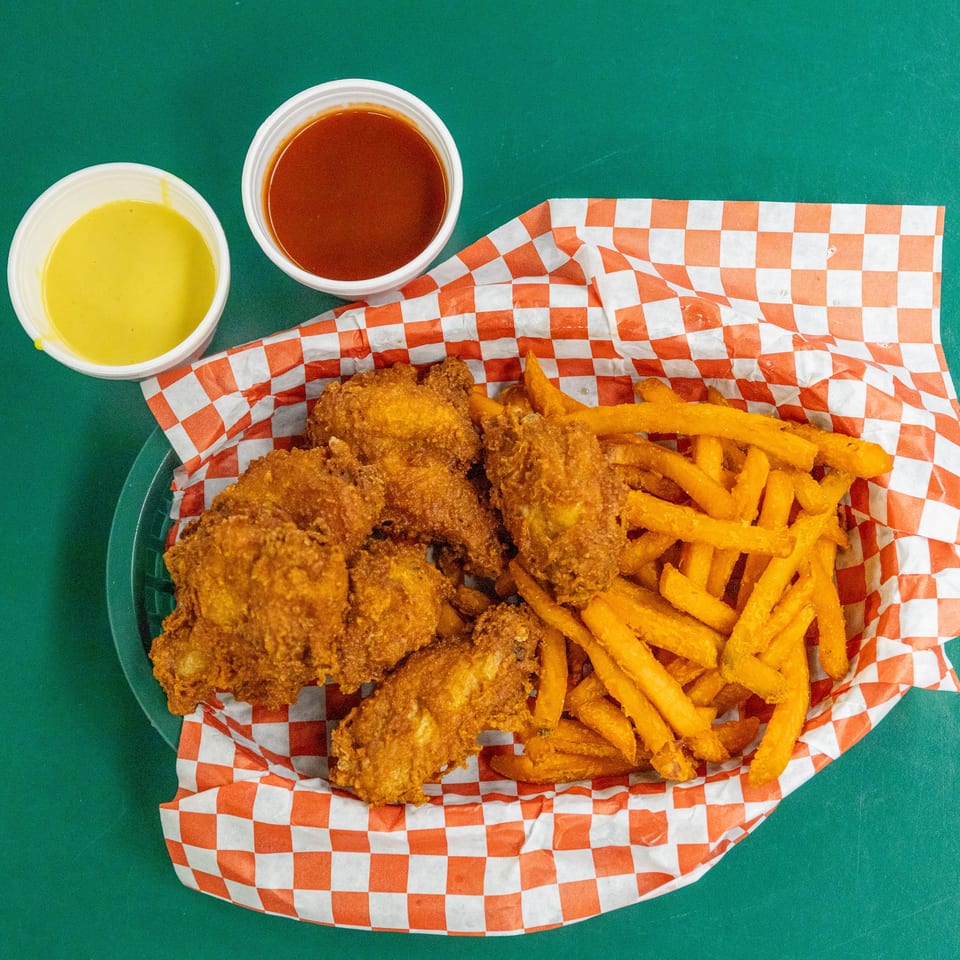 Golden fried chicken wings and sweet potato fries in a basket with two sauces.