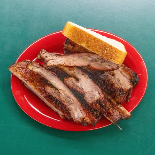 Grilled ribs with a slice of white bread on a red plate, set against a green background.