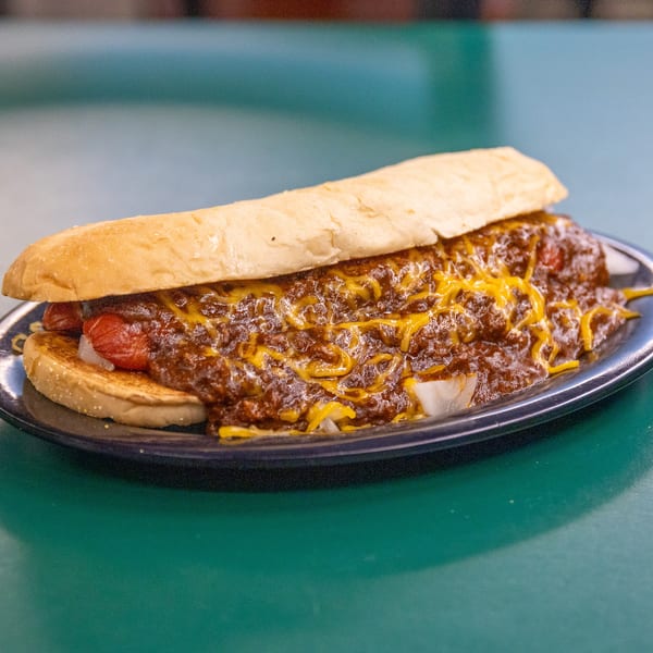 Chili cheese hot dog with onions on a dark plate, resting on a green table.