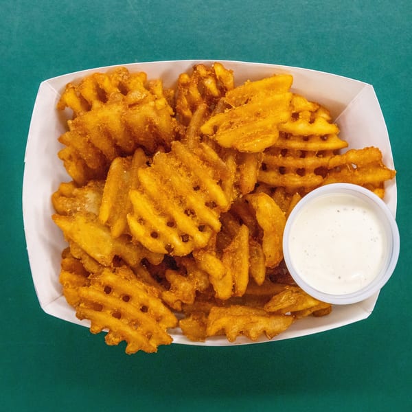 Crispy golden waffle fries in a white container with a small cup of dipping sauce.