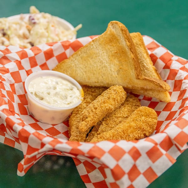 Fried tenders, toast, and tartar sauce in a checkered basket, with coleslaw in the background.